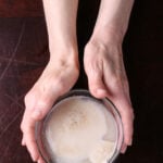 Two hands holding a bowl of yeast with sugar and water.