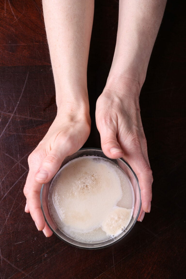 Two hands holding a bowl of yeast with sugar and water.