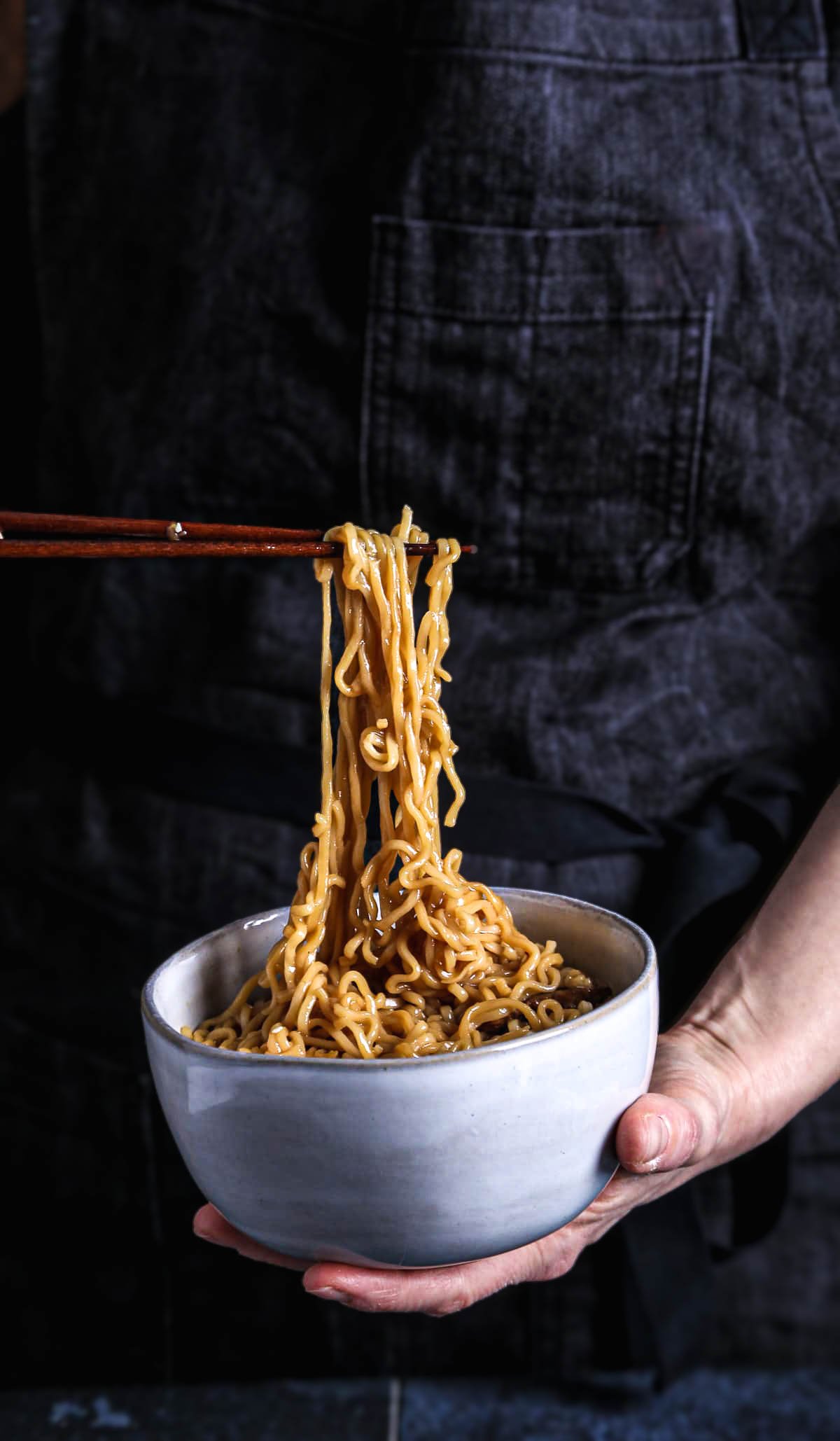 Chopsticks lifting ramen noodles from a bowl of savory vegan ramen with seitan.