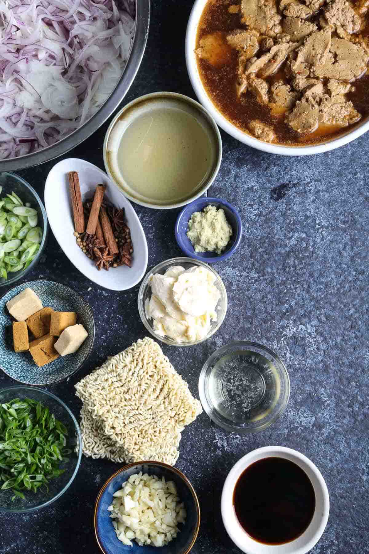Ingredients for vegan French onion ramen including onions, scallions, spices, broth, and ramen noodles.