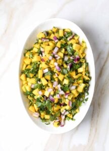 Close-up of vibrant mango salsa with cilantro and red onion in a white serving bowl.