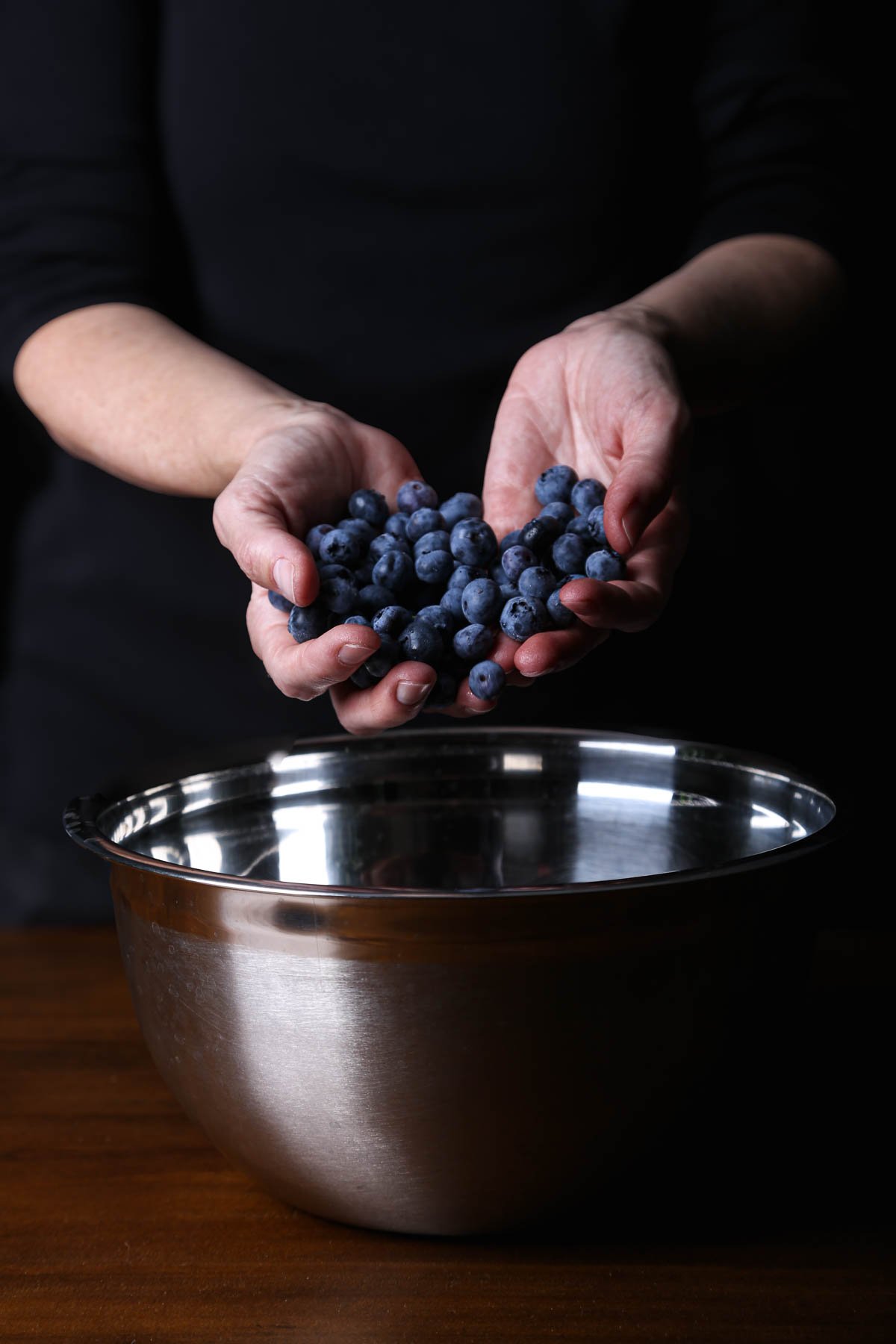 A full handful of blueberries hovering above a bowl—juicy and ripe for a vibrant berry mix.