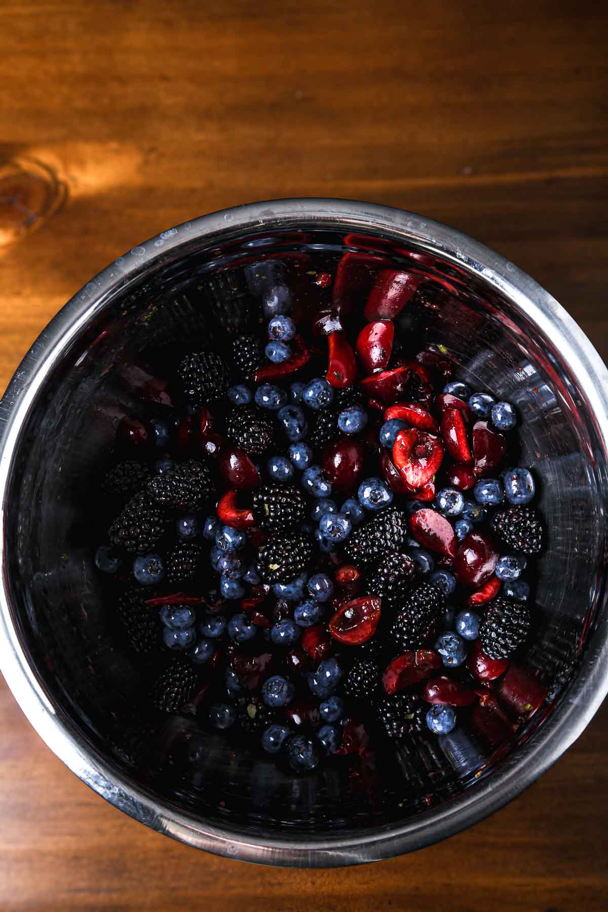 Top-down shot of a mixed berry salad with blackberries, blueberries, and cherries tossed and glistening.