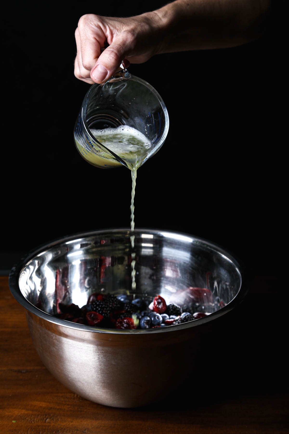 Pouring lime juice into a bowl of berries in a steel prep bowl.