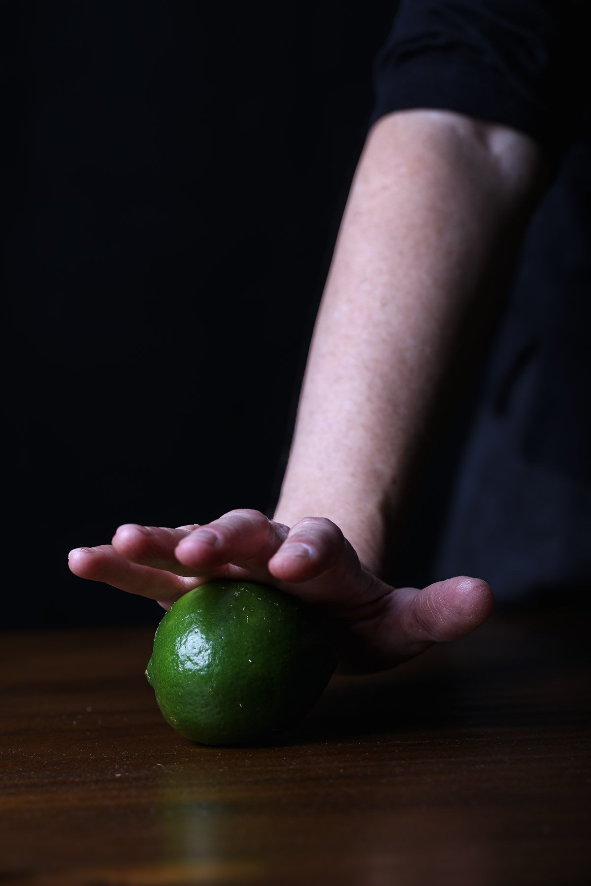 Rolling a fresh lime on a wooden surface; an essential step to prep the citrus for juicing.