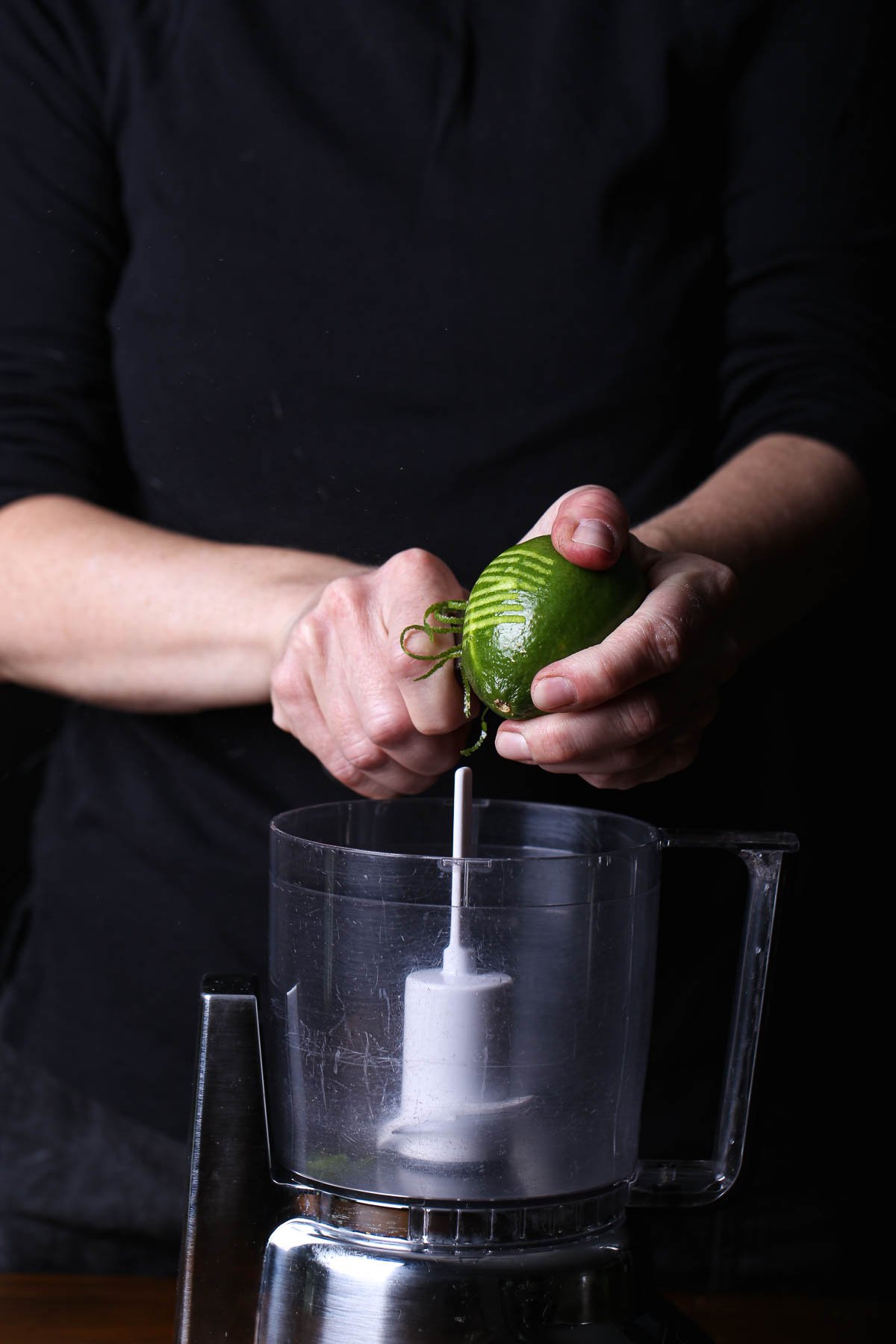 Zesting a lime directly over a food processor—citrus oil and lime zest brightening the dressing.
