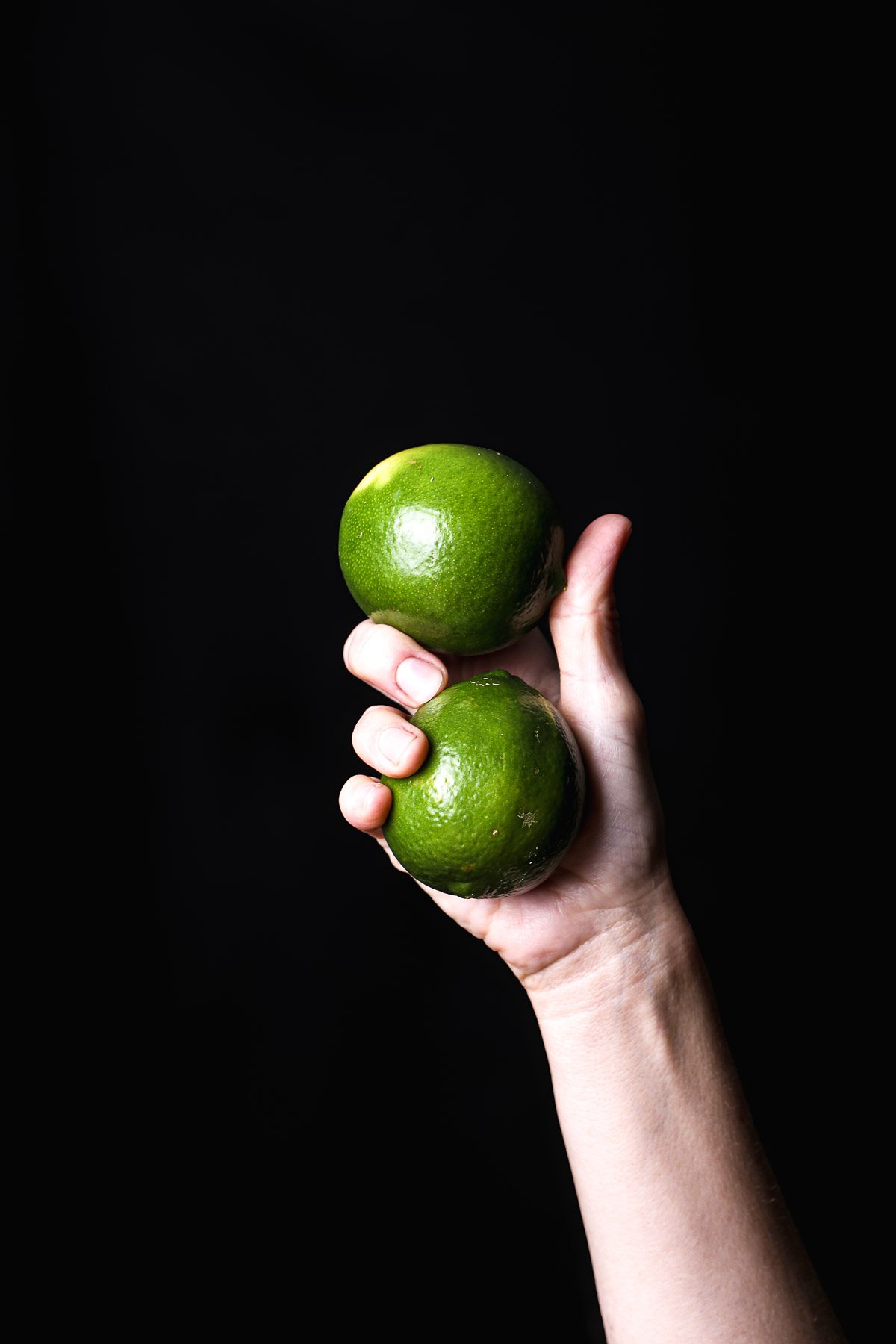 Holding two whole limes against a black backdrop—bright, bold, and about to be juiced.