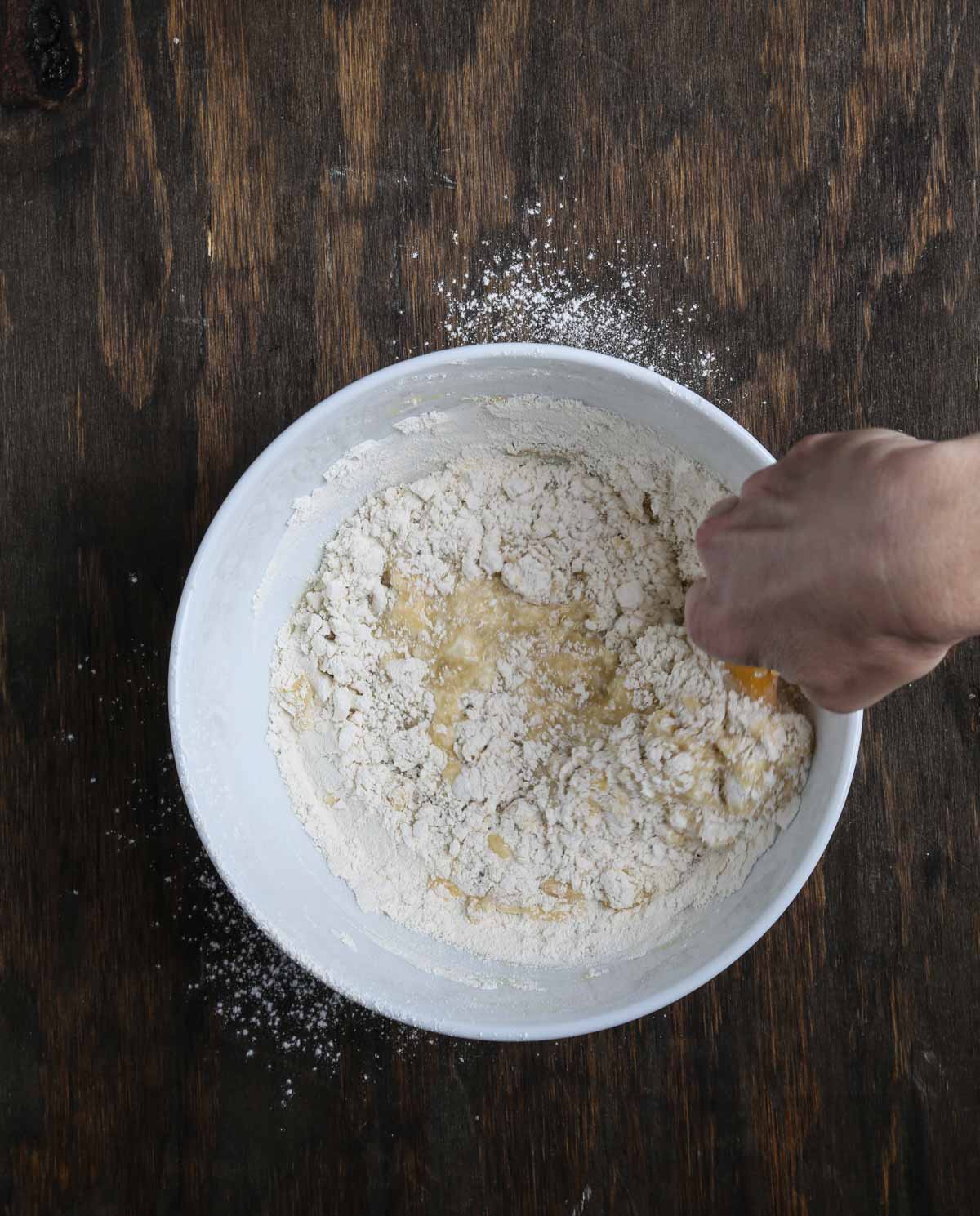 Stirring dry and wet ingredients together by hand to make vegan berry cobbler batter.