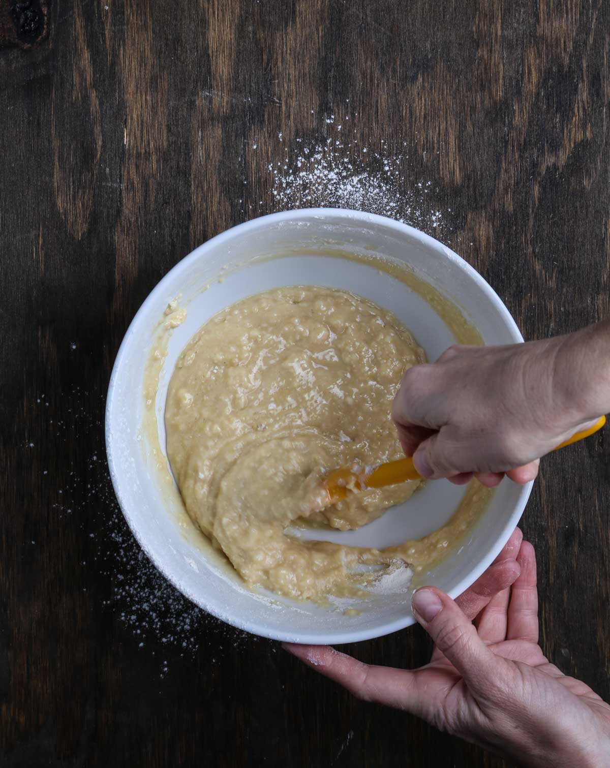 Vegan cobbler batter being gently mixed by hand in a white bowl.