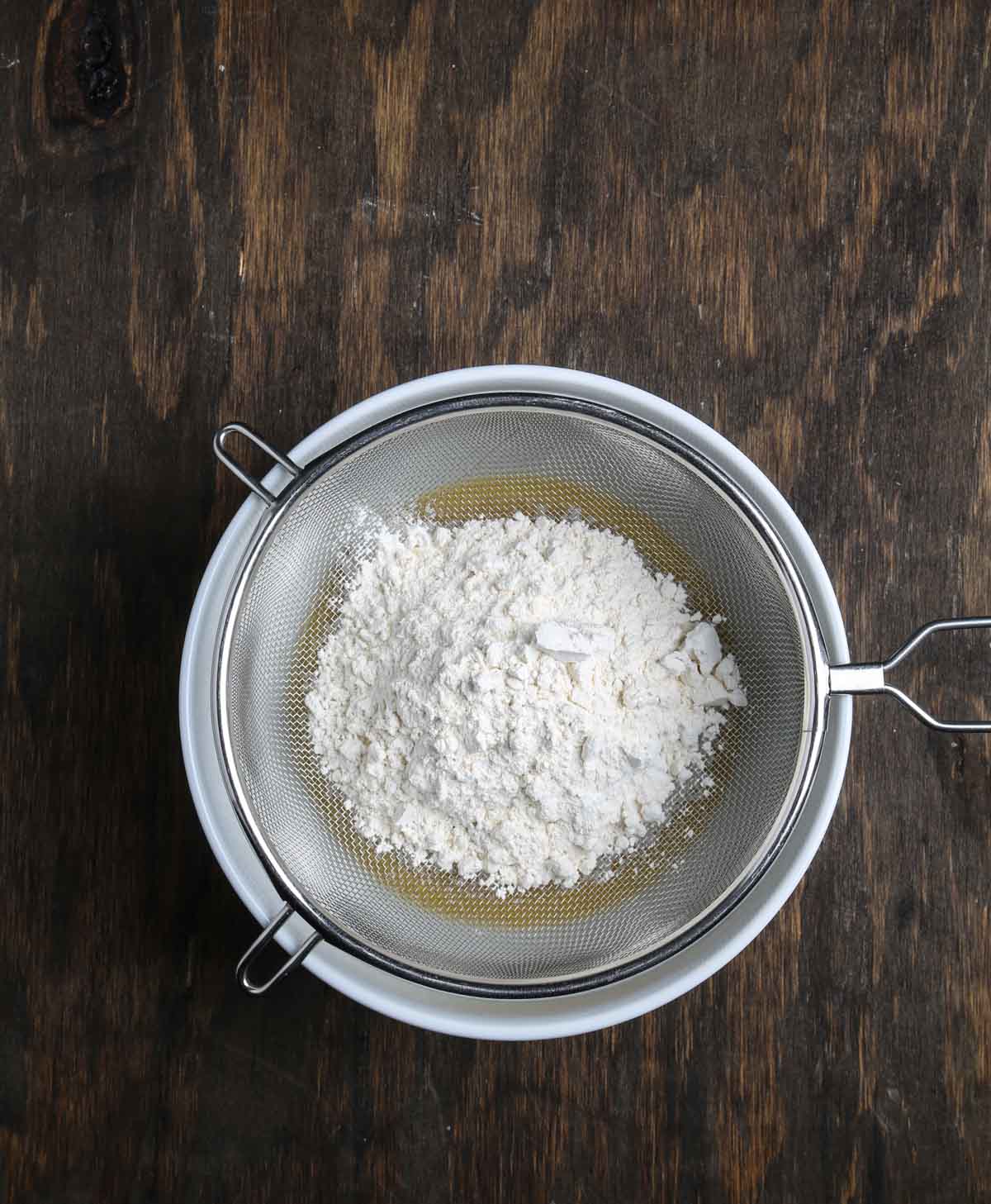Sifting flour and dry ingredients into a bowl of wet ingredients for vegan cobbler batter.