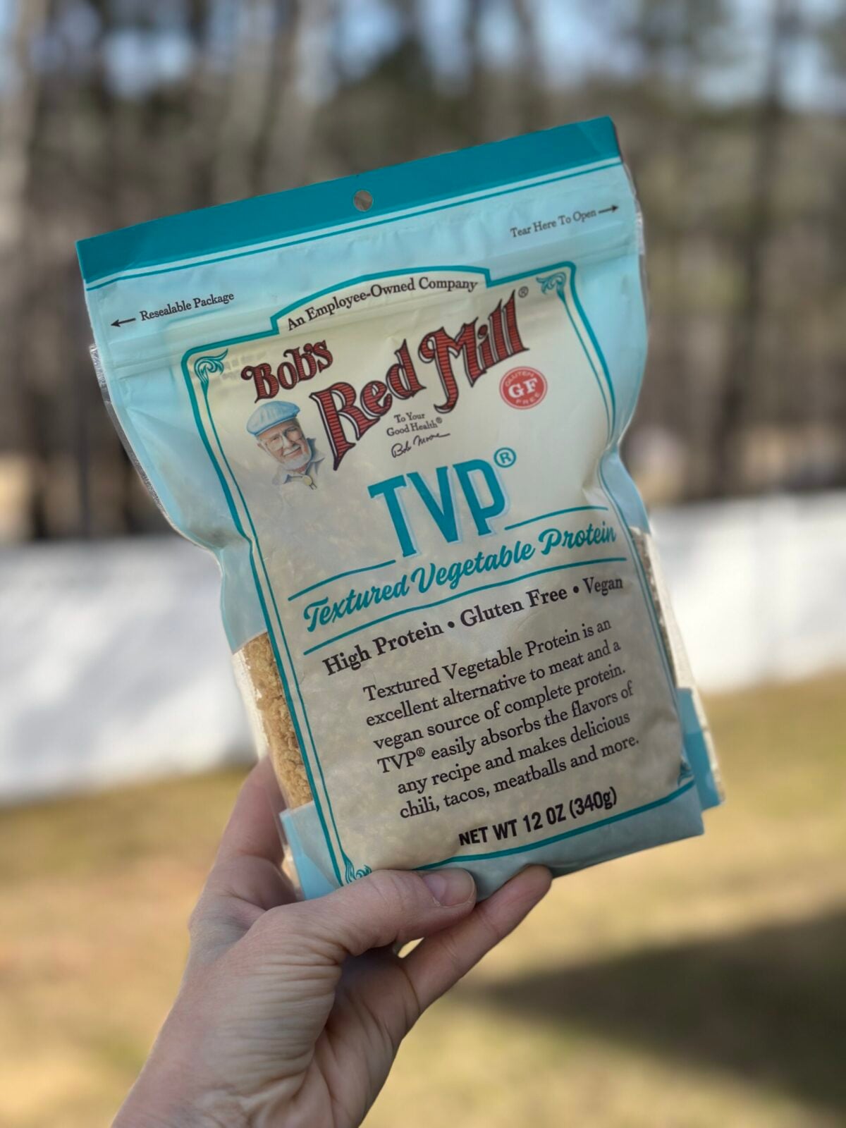 A hand holding a bag of Bob's Red Mill TVP (Textured Vegetable Protein), a shelf-stable vegan protein source.