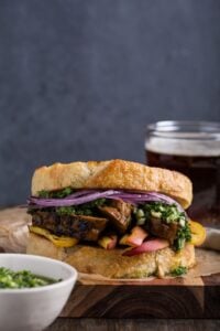 Vegan steak sandwich on crusty bread with grilled plant-based slices, red onion, and greens.