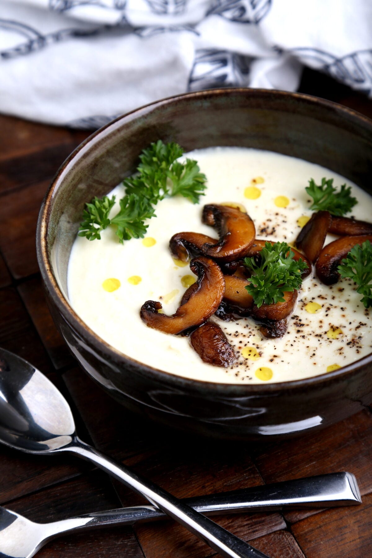 Bowl of creamy vegan cauliflower and cashew soup garnished with mushrooms and herbs.
