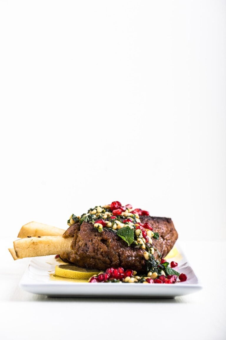 Vegan steak served with herbs, pomegranate, and lemon on a white plate.