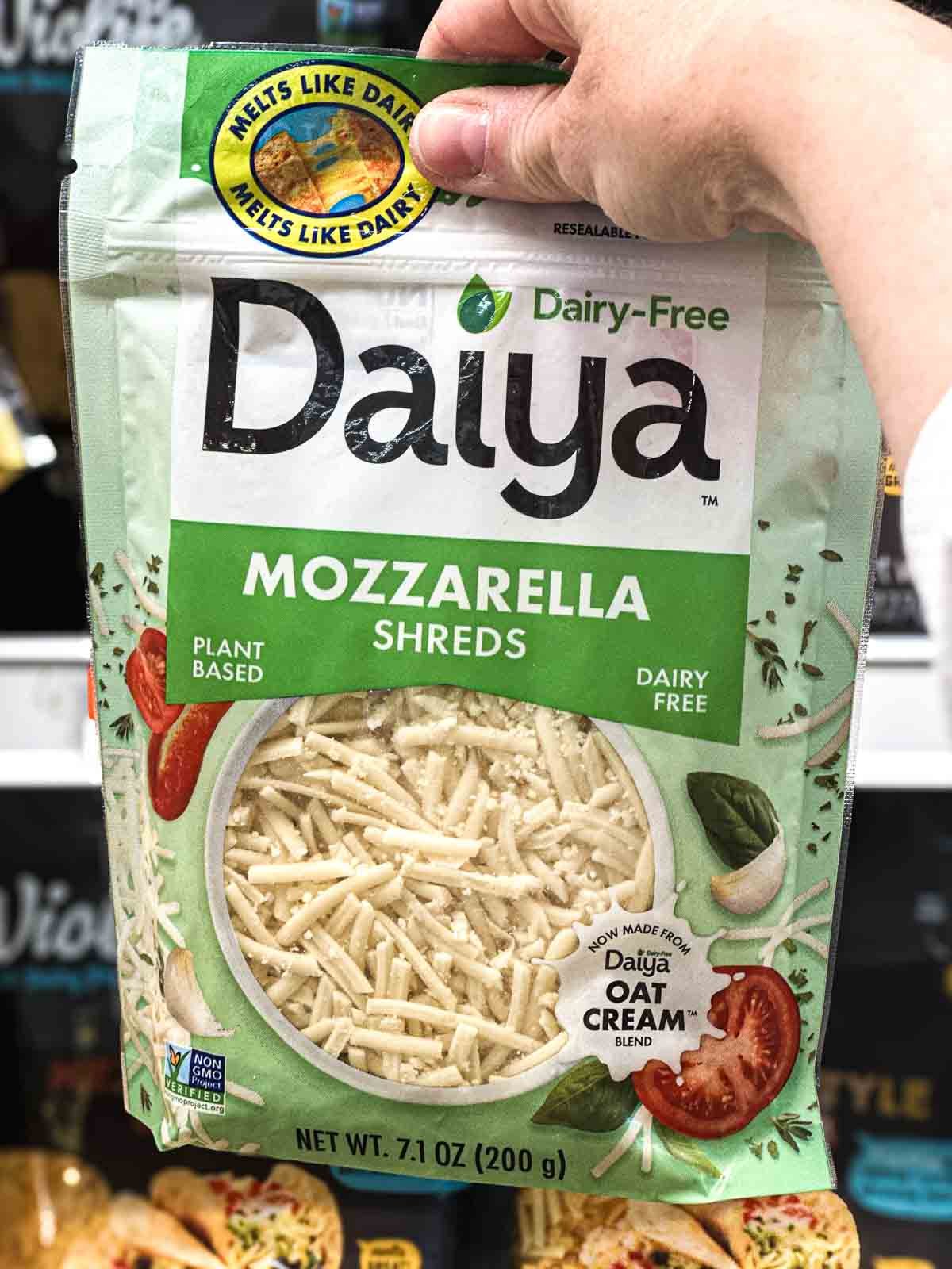 Bag of Daiya plant-based mozzarella shreds made with oat cream, held in front of grocery shelf.