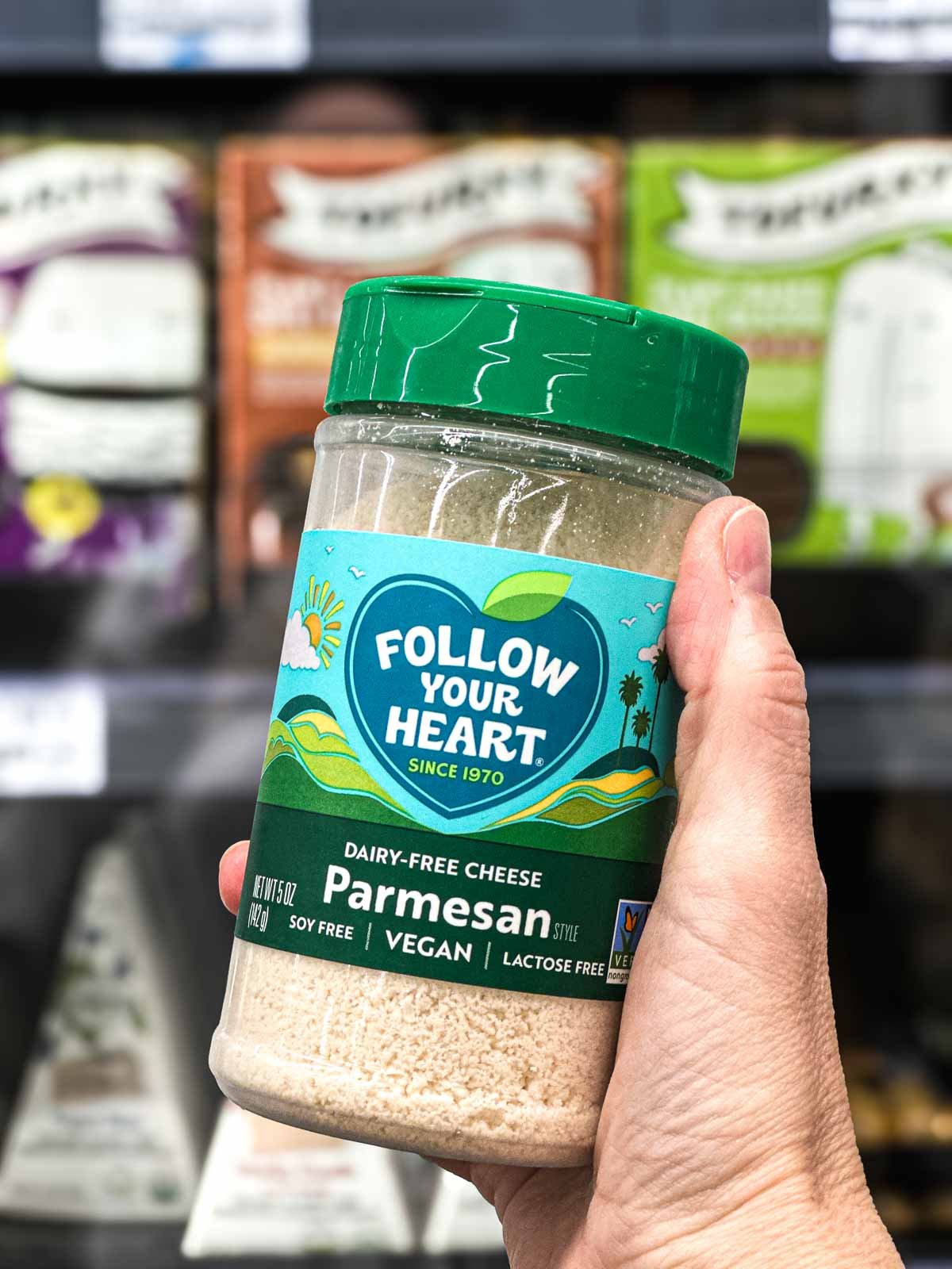 Close-up of Follow Your Heart dairy-free parmesan sprinkles in a plastic shaker bottle, photographed in a grocery store aisle.