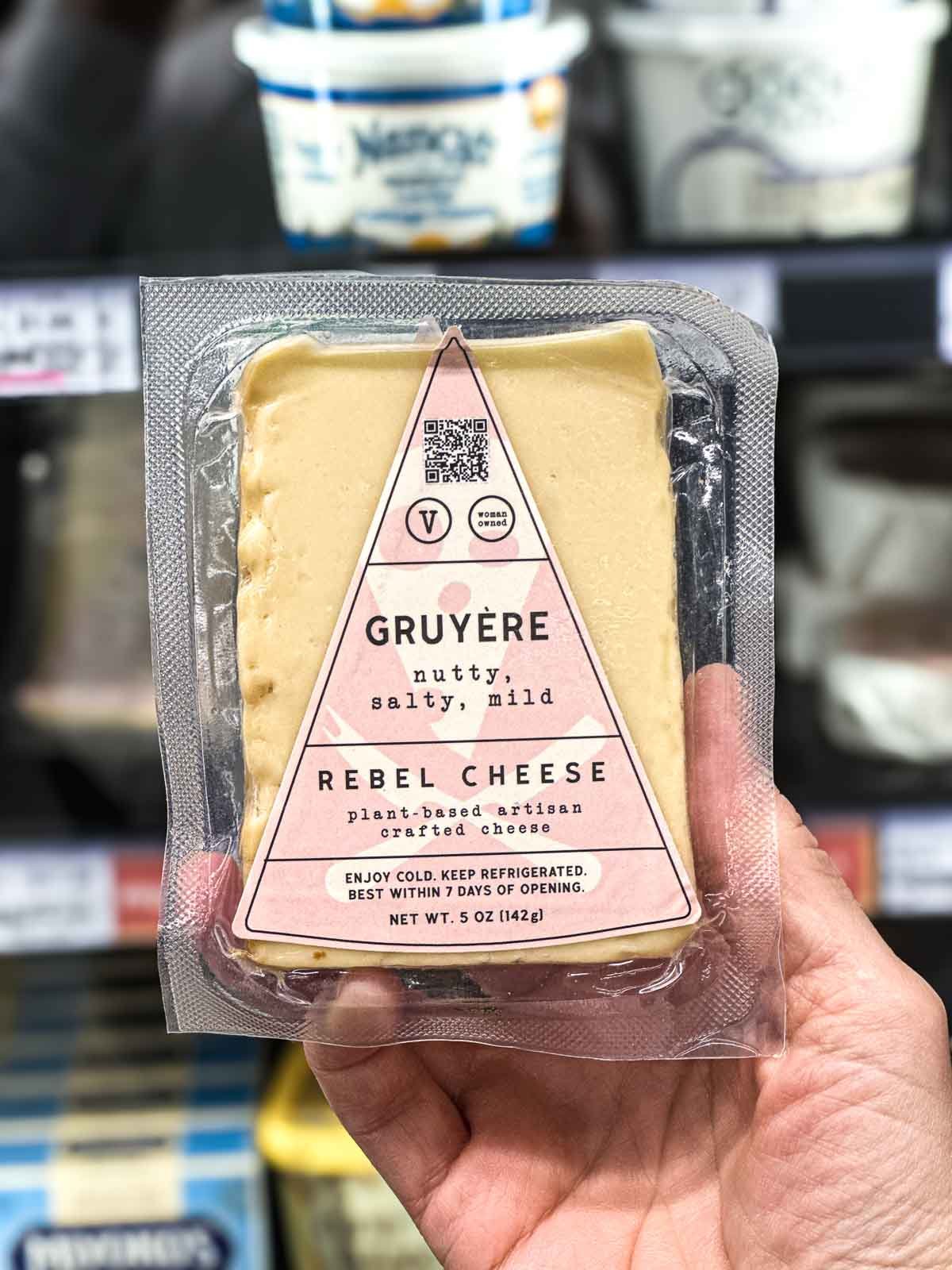 Rebel Cheese Gruyère vegan cheese in pink triangle packaging with nutty, salty, and mild flavor notes.