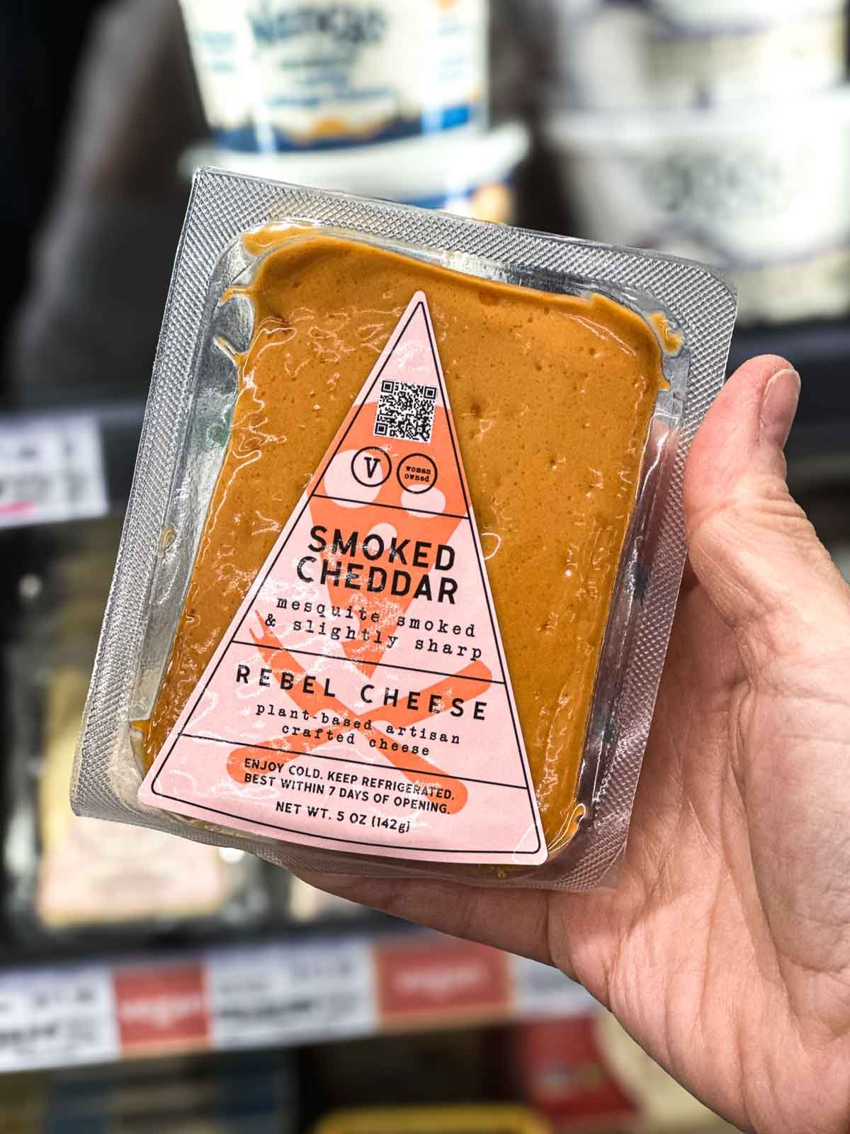 Rebel Cheese vegan smoked cheddar block in plastic package, photographed in grocery store dairy section.