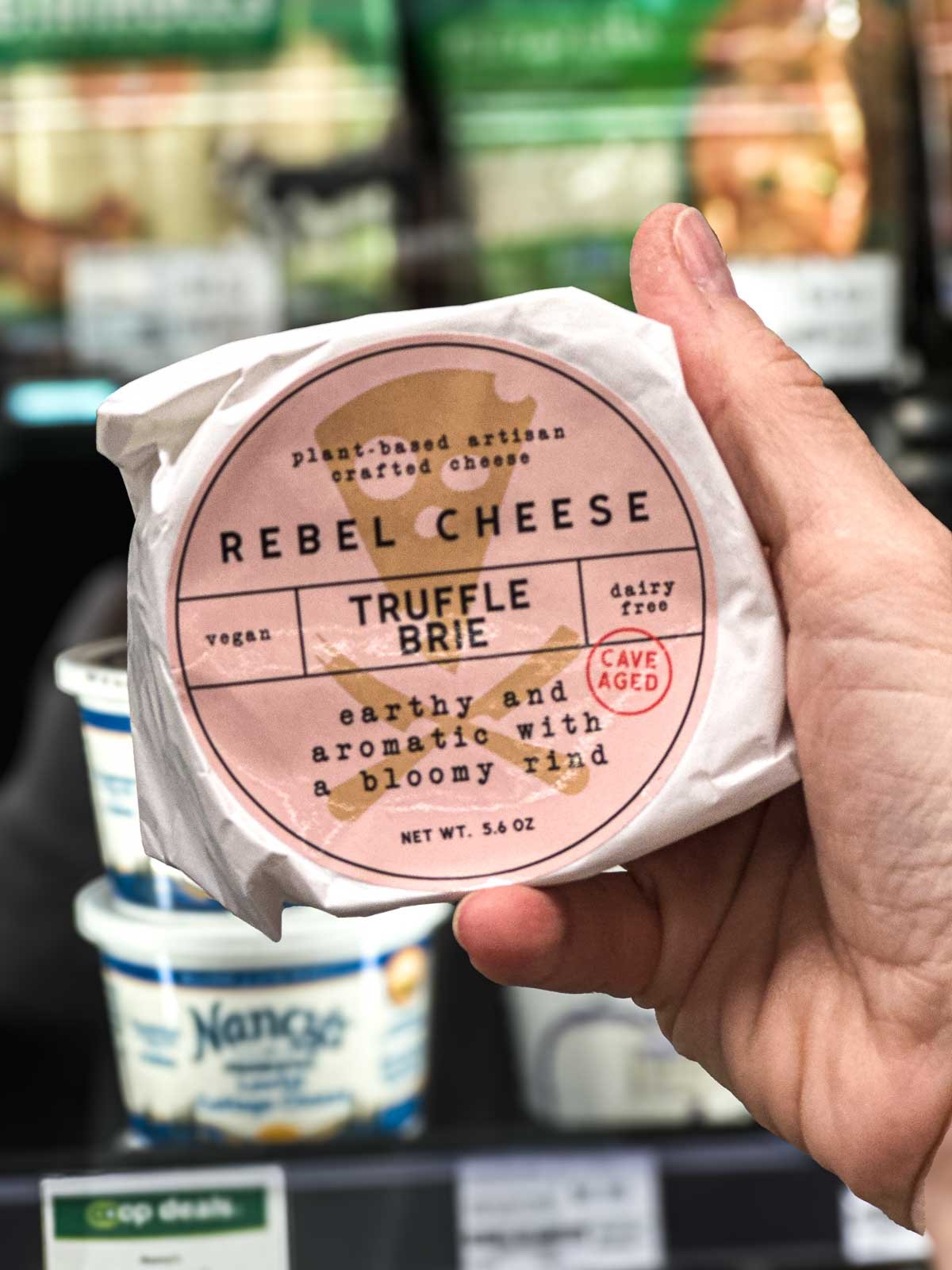 Rebel Cheese Truffle Brie round wrapped in paper, a cave-aged vegan cheese with an earthy bloomy rind.