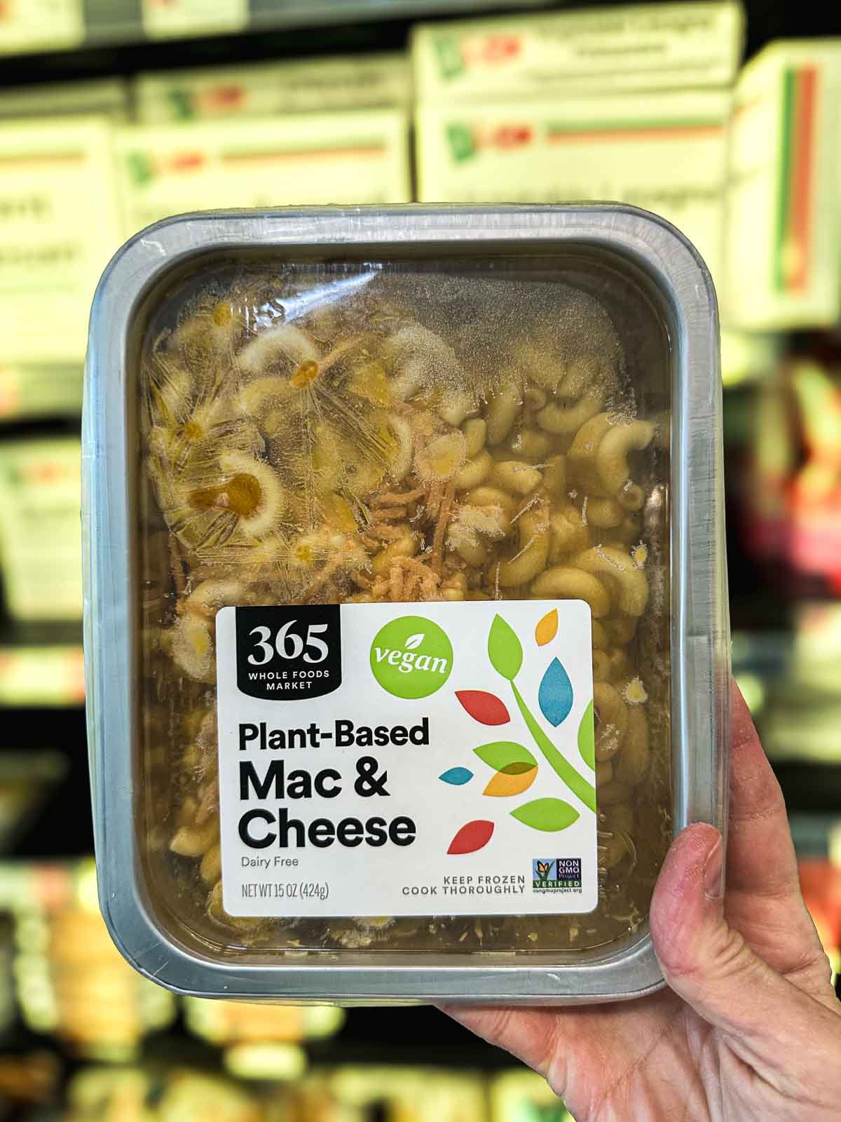 Whole Foods 365 vegan mac and cheese in a frozen tray in the vegan frozen foods section with visible pasta inside the clear packaging.