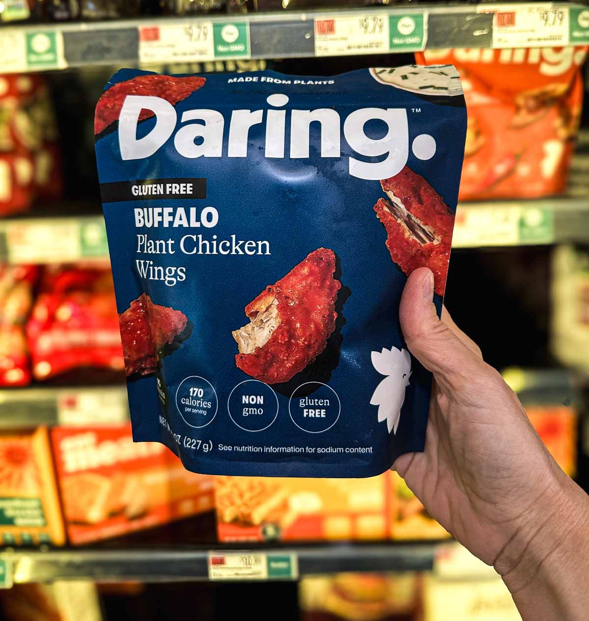 Daring Buffalo Plant Chicken Wings in a navy blue bag, held up in front of a freezer aisle display.
