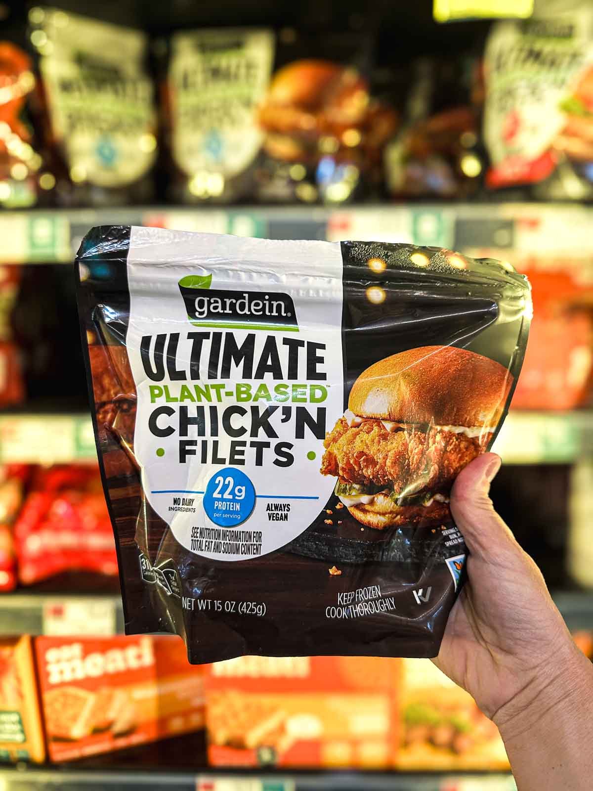 Gardein Ultimate Plant-Based Chick’n Filets packaging held in front of freezer shelf, featuring crispy vegan chicken sandwich on the label.