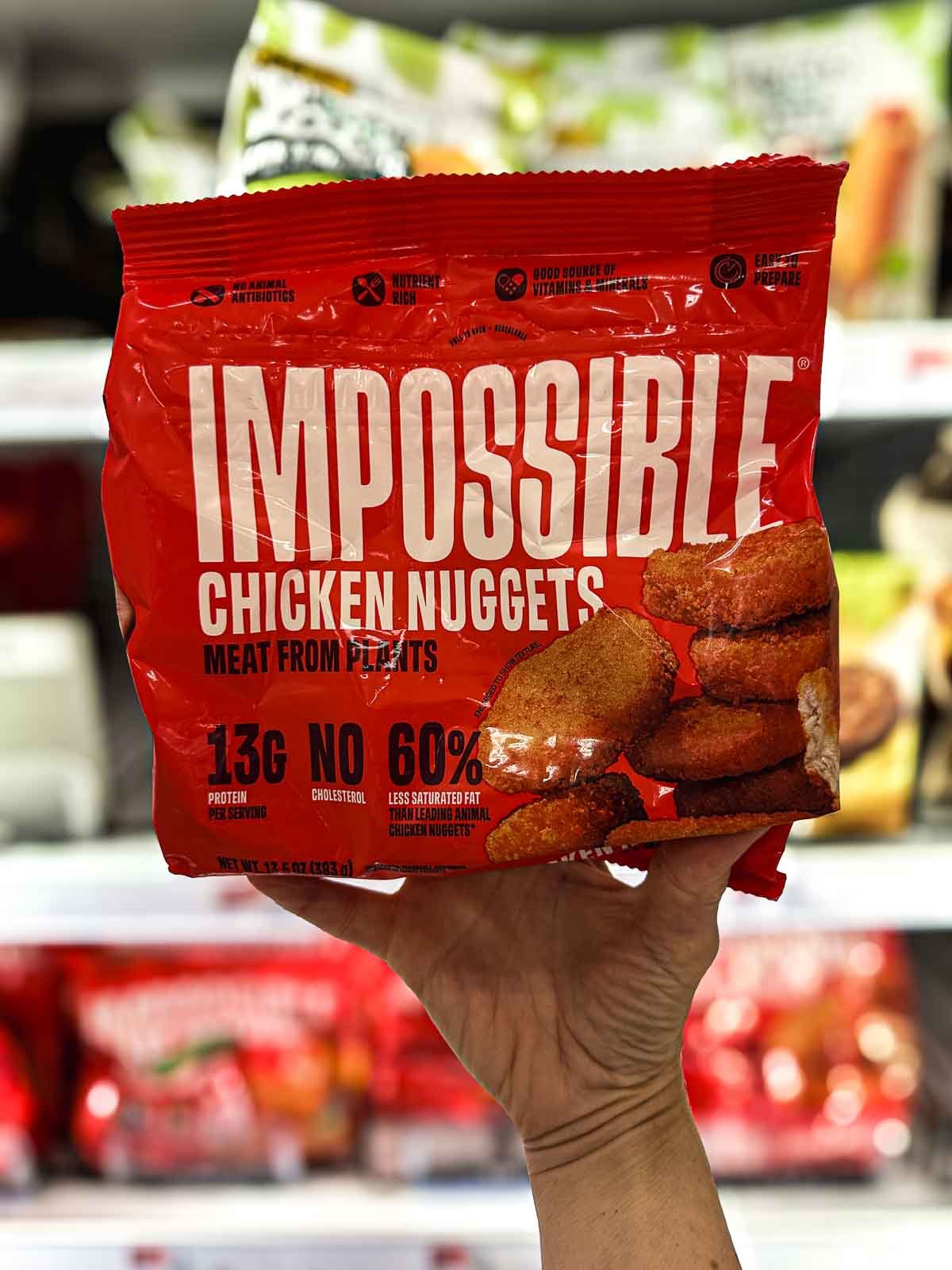 Impossible Chicken Nuggets bag featuring crispy plant-based nuggets with a bright red background.