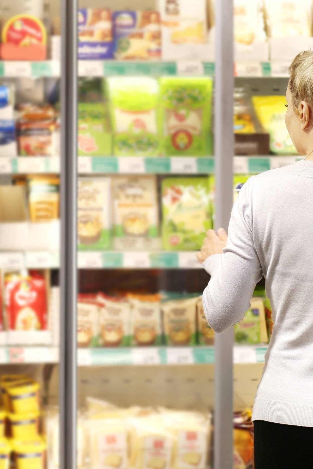 Woman selection foods in the freezer section of a grocery store.