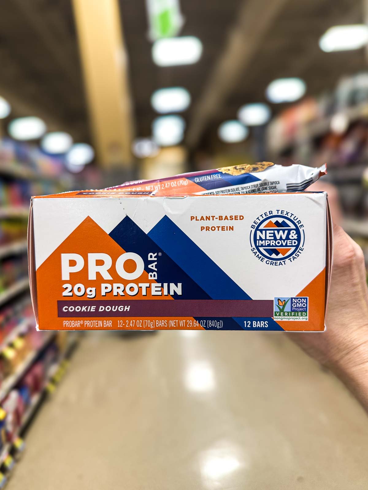 A box of PROBAR cookie dough protein bars with 20 grams of plant-based protein, displayed in a grocery aisle with bright orange and blue packaging.