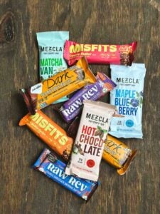 Top vegan protein bars like Mezcla, Misfits, Raw Rev, and NuGo displayed flat on a wooden surface.