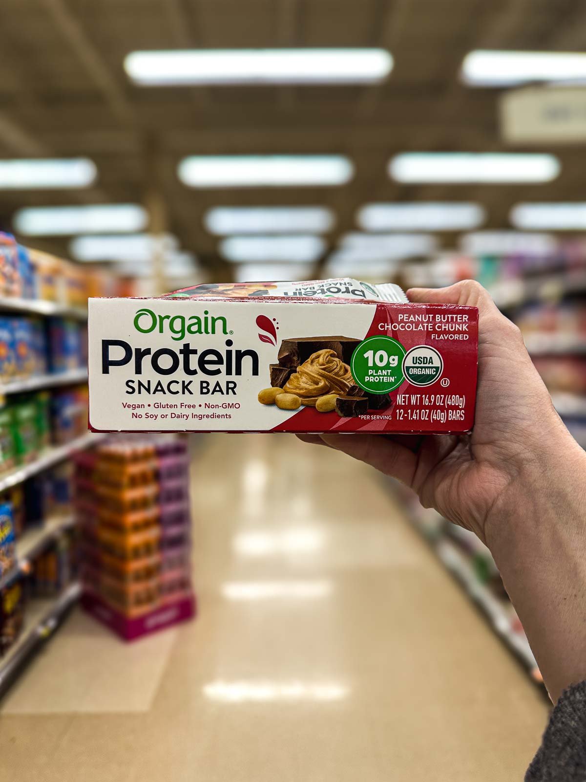 Box of Orgain vegan protein bars in a grocery store aisle, Peanut Butter Chocolate Chunk flavor shown.