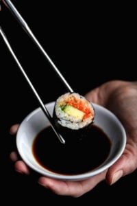 Chopsticks dipping a vegan sushi roll into soy sauce for rich umami flavor.