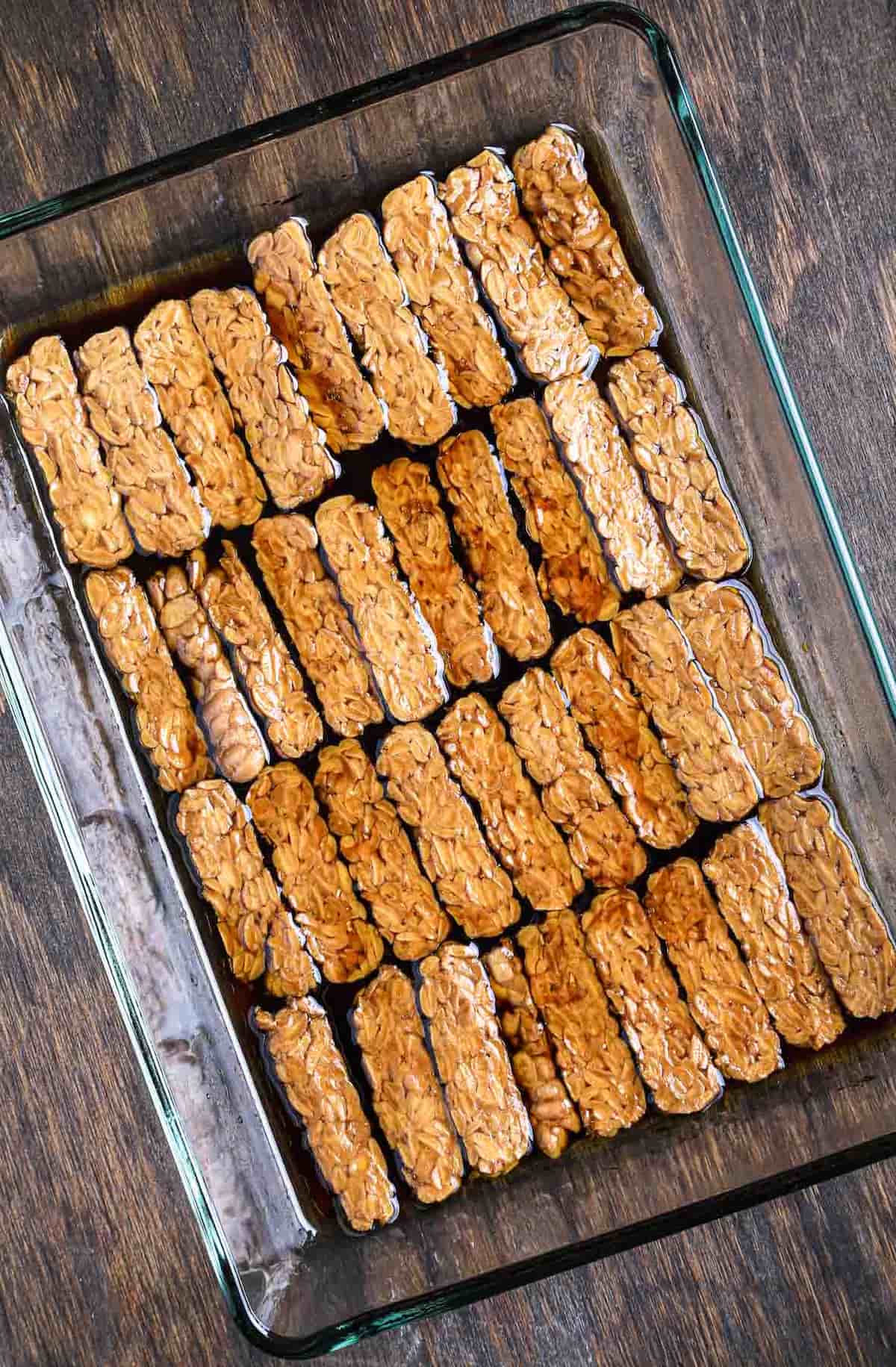 Thin tempeh slices soaking in a smoky maple soy marinade for vegan tempeh bacon.