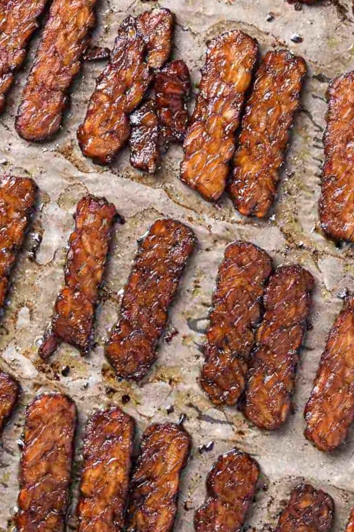 Crispy baked tempeh bacon on a parchment-lined baking sheet, caramelized and smoky from a maple-tamari marinade.