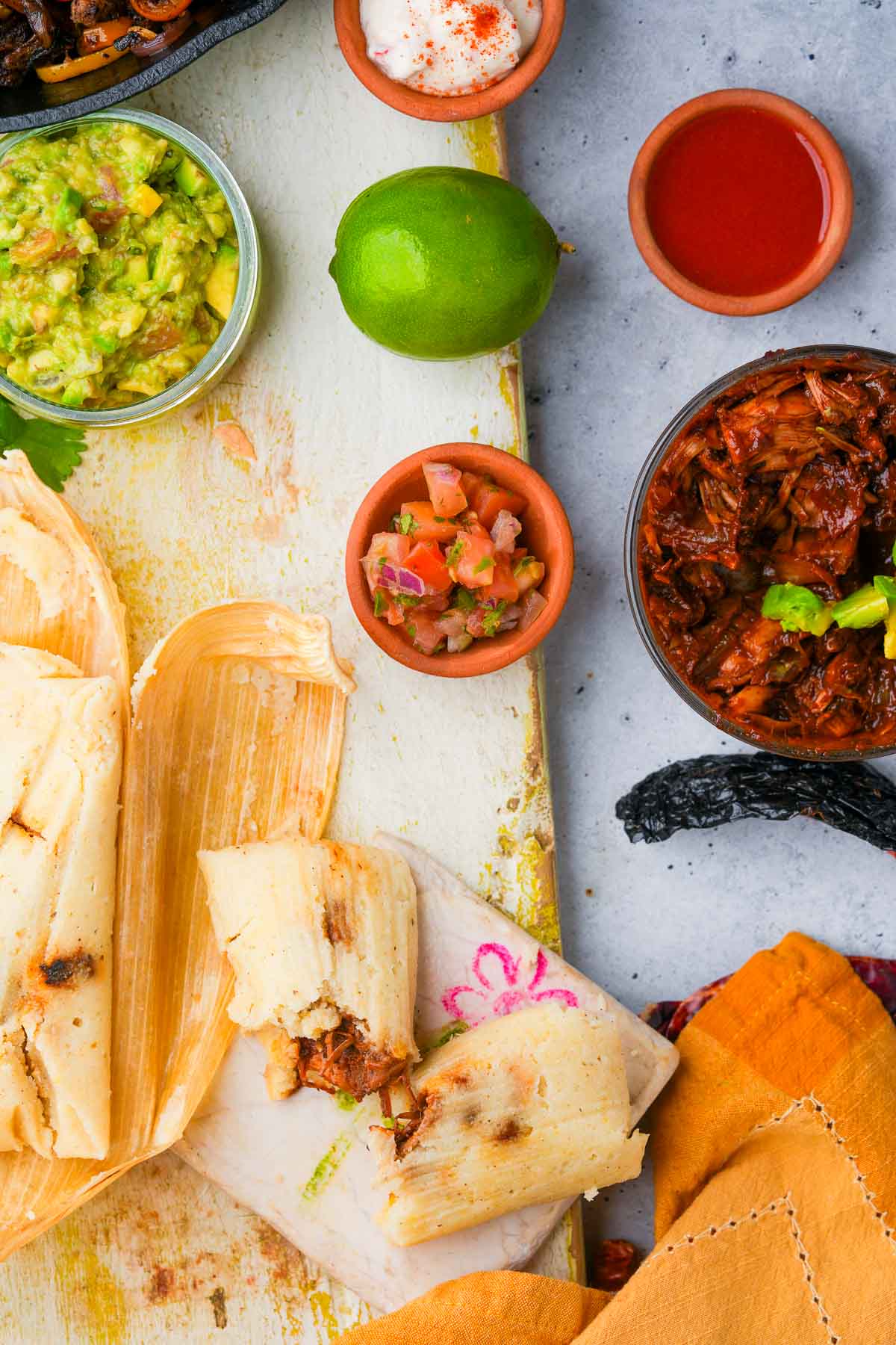 Vegan ancho chili jackfruit tamales served with guacamole, salsa, and lime on a rustic board.
