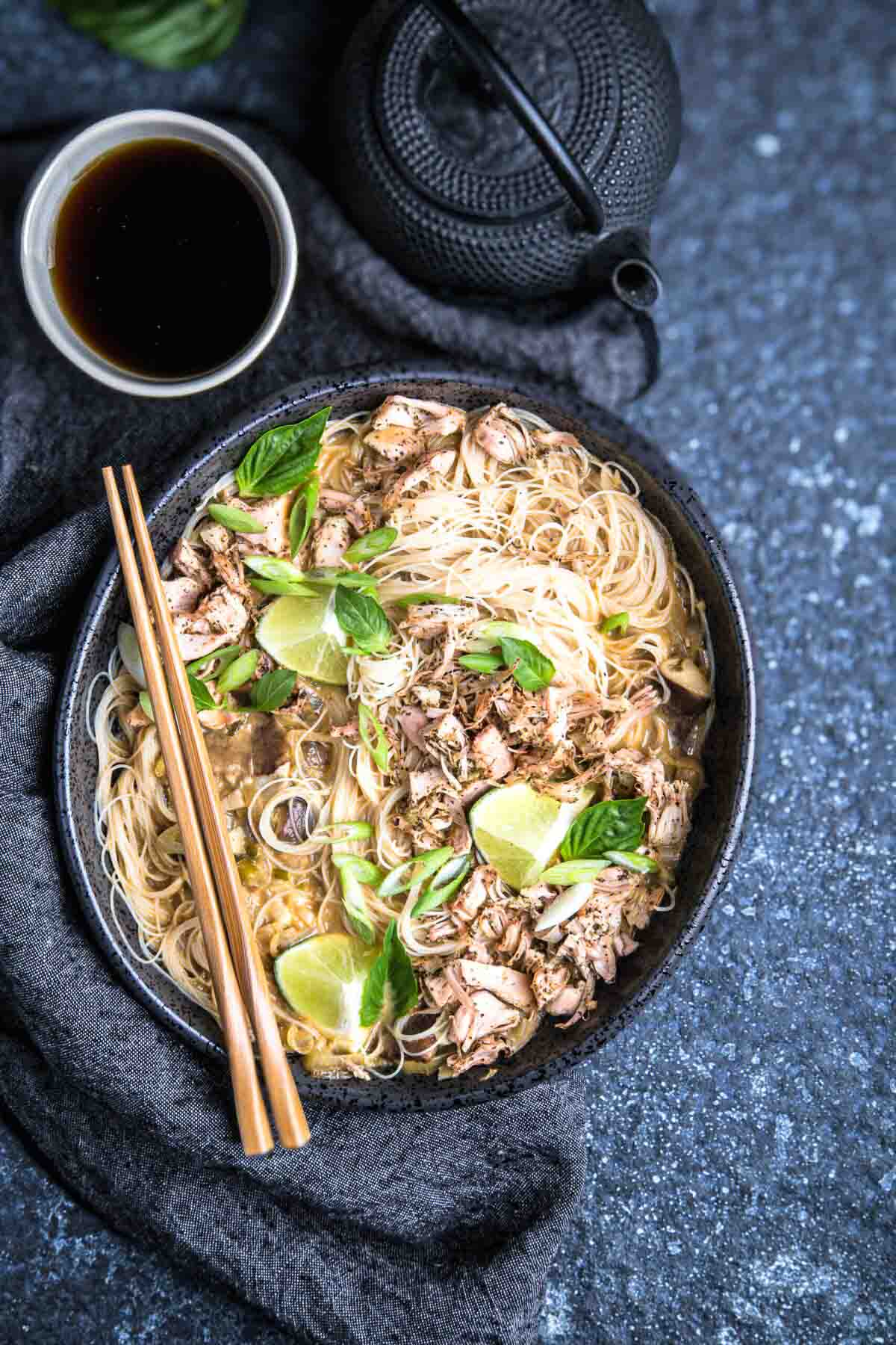 Bowl of vegan crab coconut soup made with jackfruit, noodles, lime, and herbs on a dark stone background.