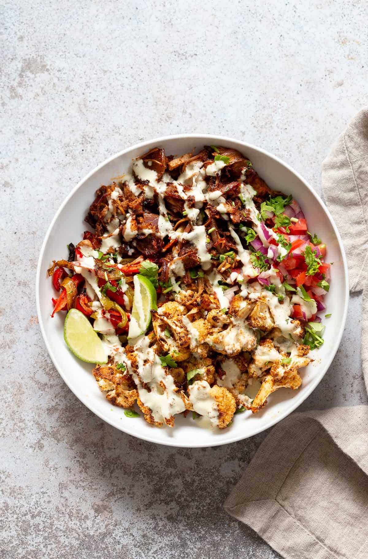 Lime roasted veggie and jackfruit salad drizzled with creamy dressing and fresh herbs.