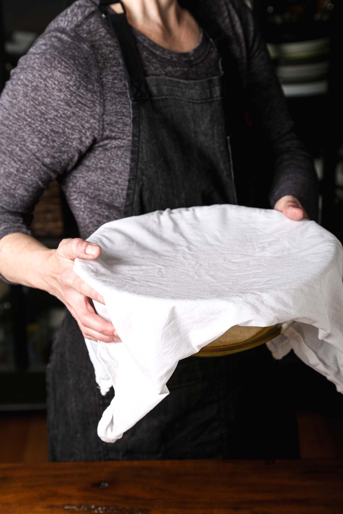 Hands holding a bowl of bread dough with a towel for the first rise.