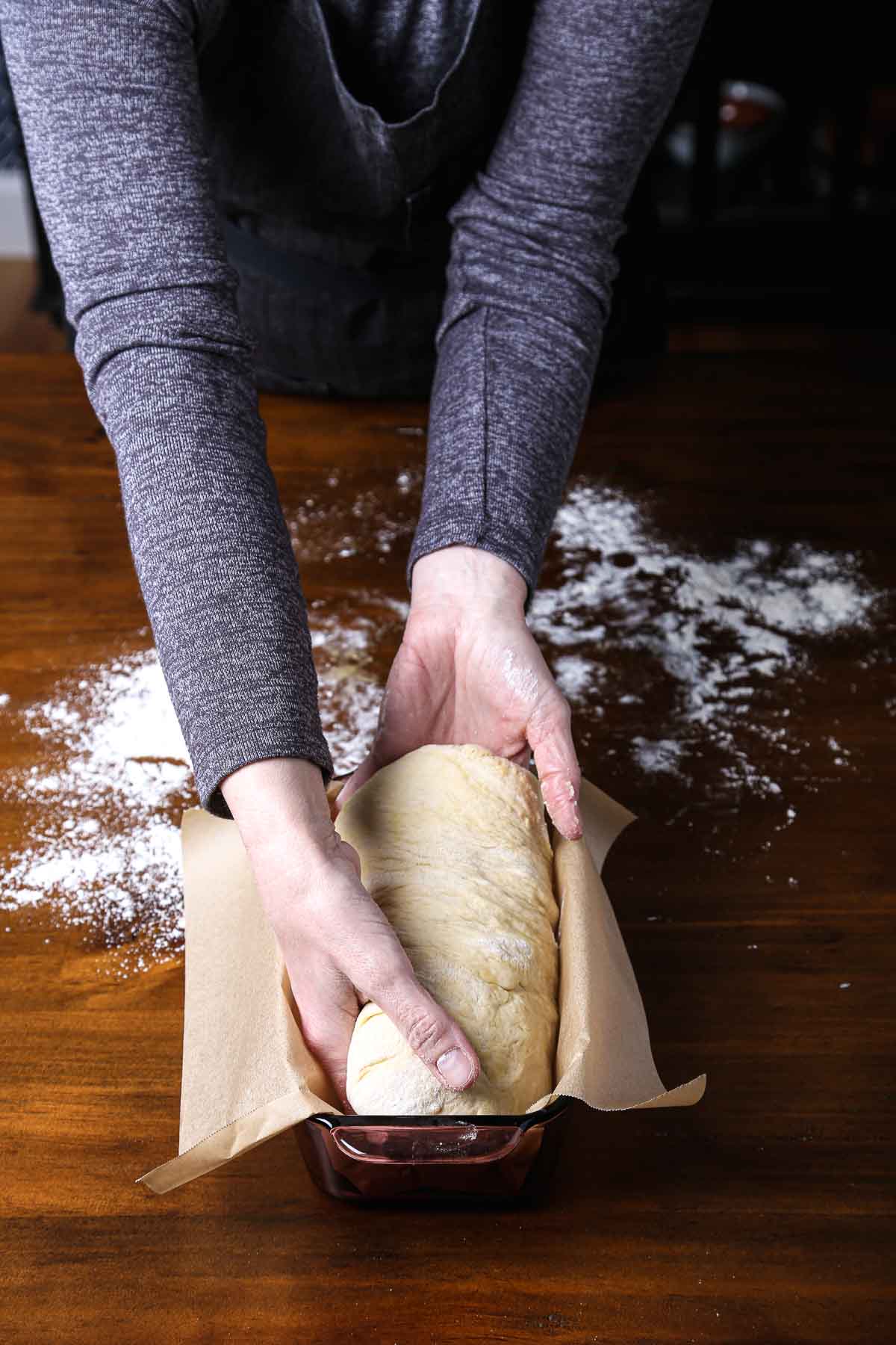 Shaped dough being placed seam-side down into a parchment-lined loaf pan.