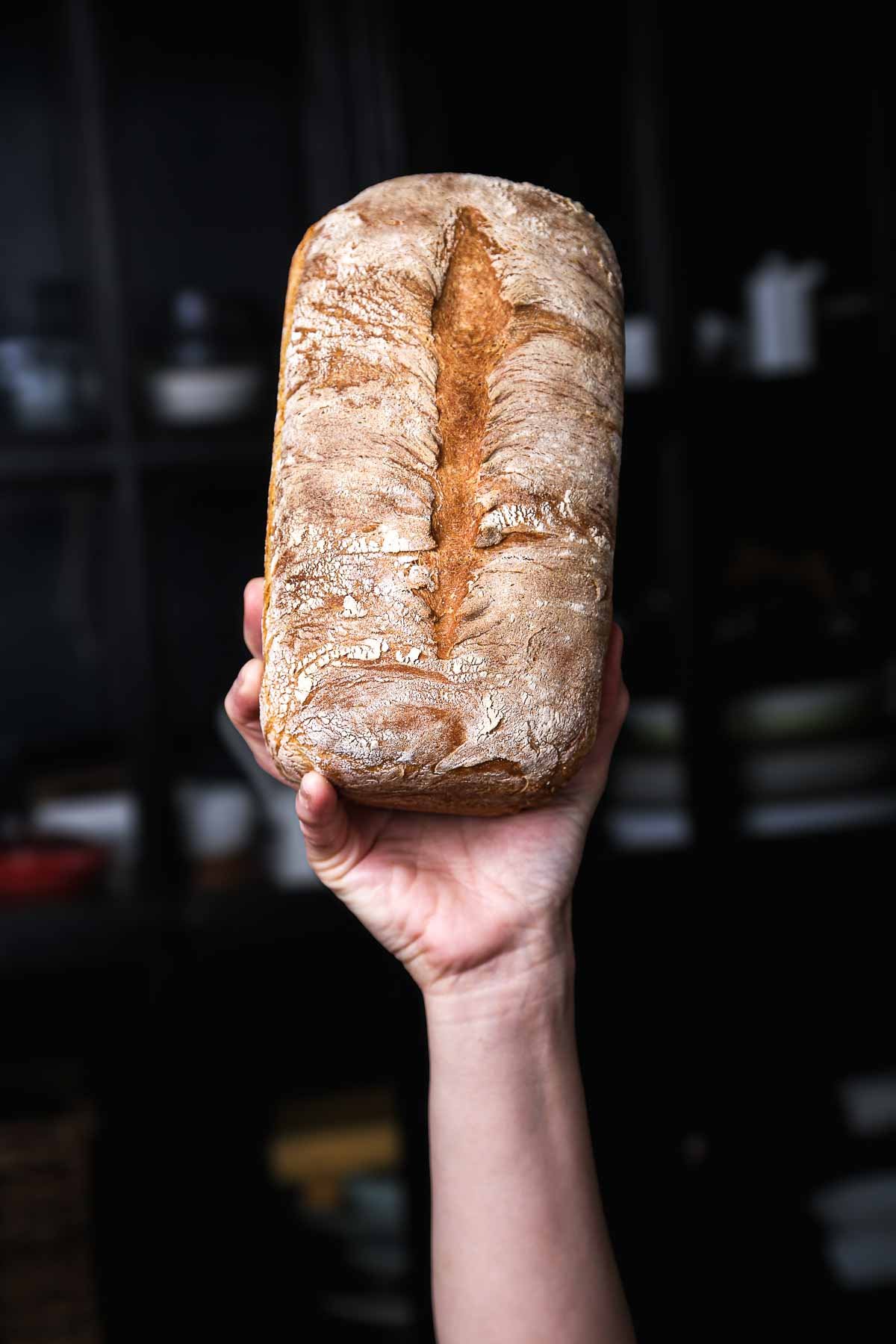 Freshly baked sandwich bread loaf held up to show its crisp crust and center score—a soft, sturdy homemade sandwich bread recipe.