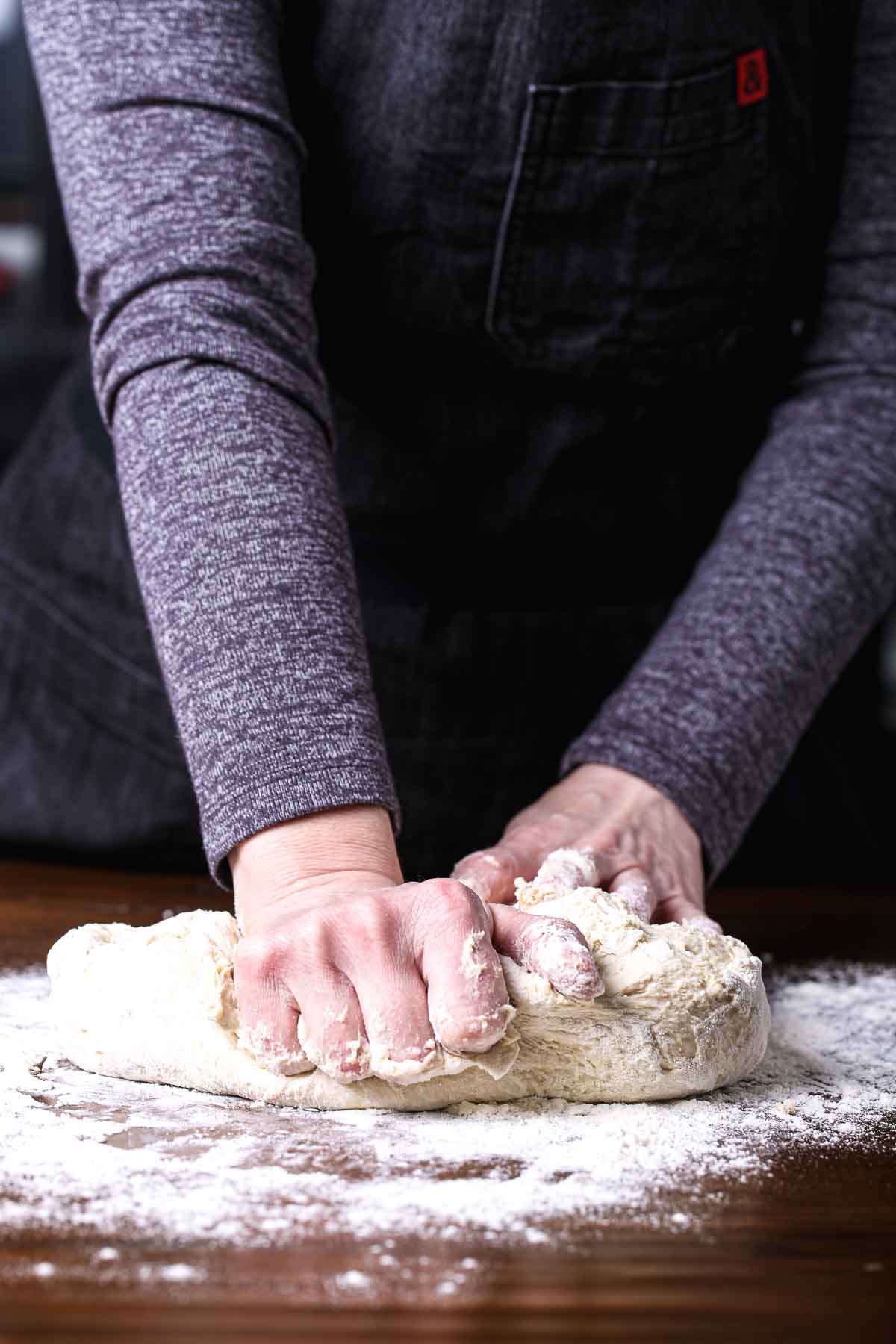 Hands kneading bread dough on a floured work surface.