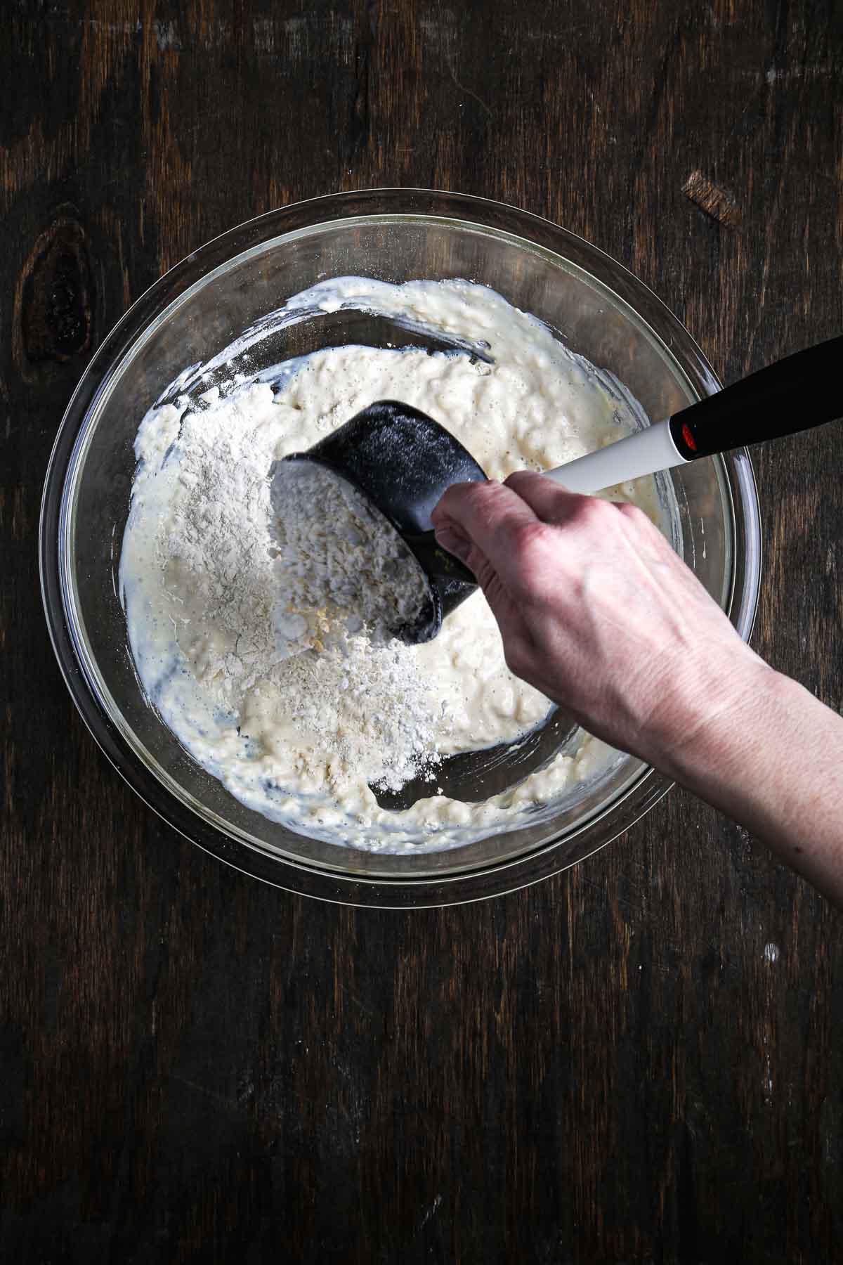 Hand pouring another scoop of flour into the partially mixed sandwich bread dough.