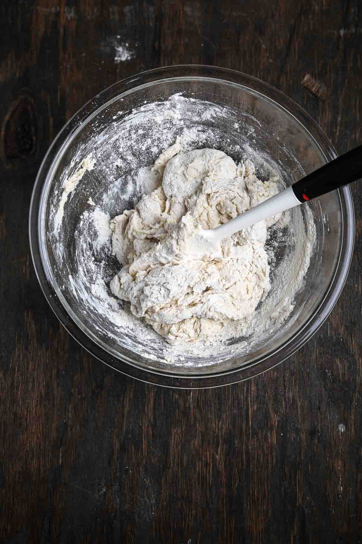 Shaggy, floury dough forming in a glass bowl before kneading.