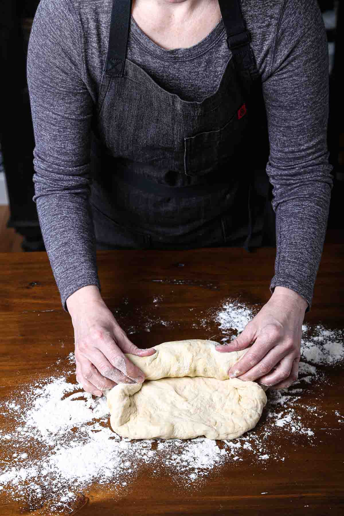 Hands rolling up sandwich bread dough, tucking end seams in.