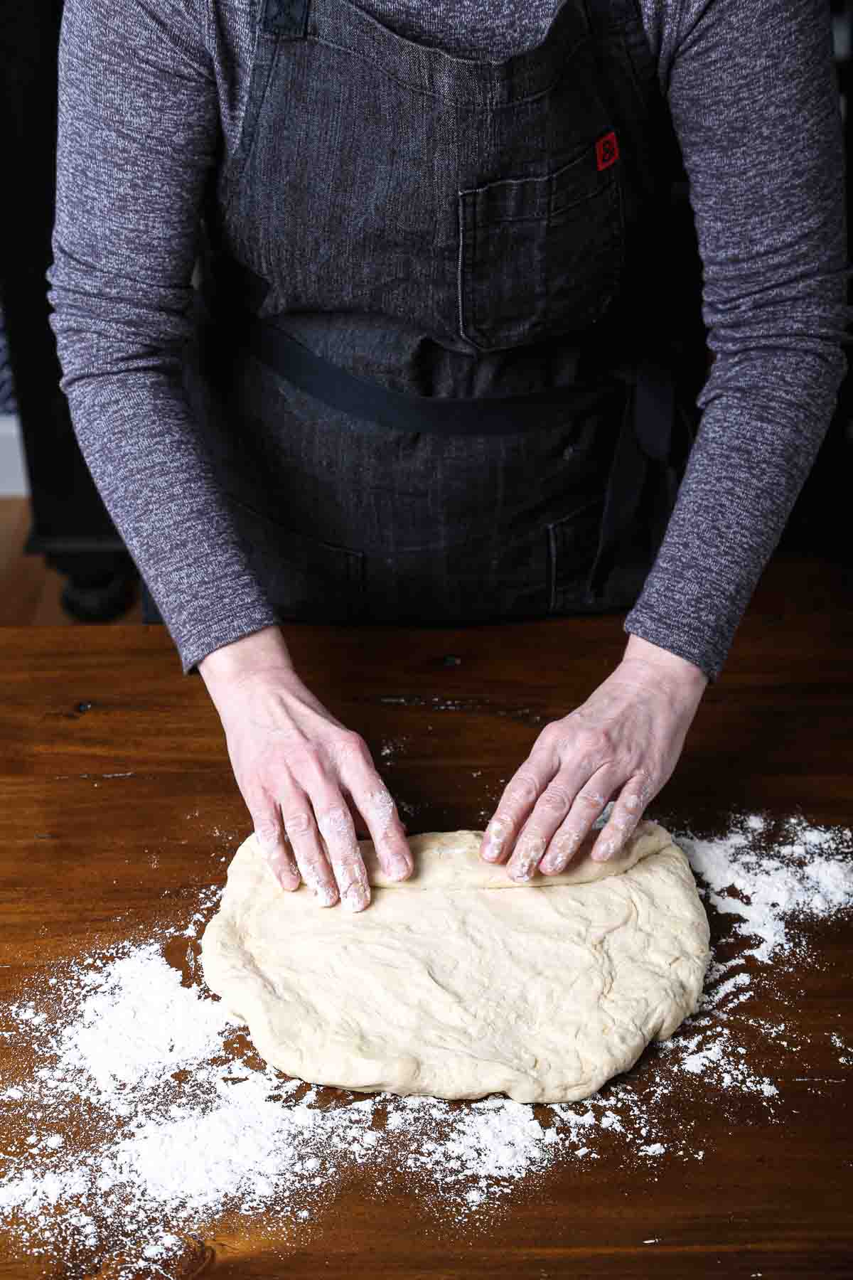 Hands folding the bottom edge of the dough up to begin rolling it into a tight loaf.