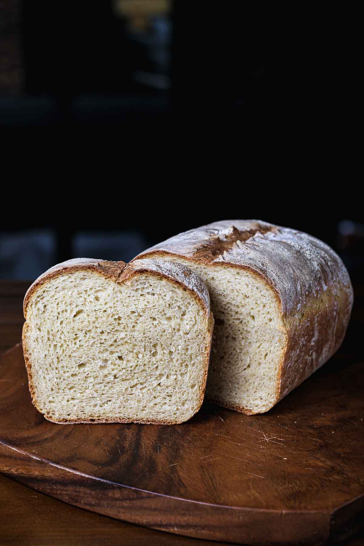 Homemade sandwich bread sliced on a wooden board, showing a soft, even crumb and lightly golden crust.