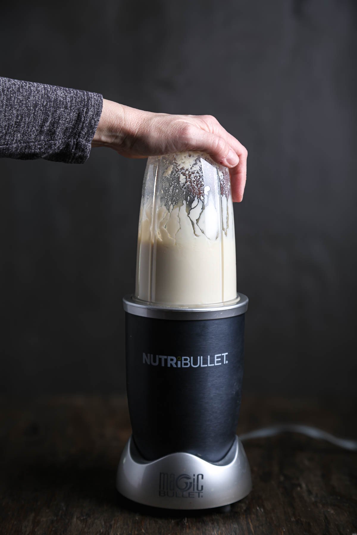 A hand holding the top of a small blender while blending silken tofu with apple cider vinegar and salt.