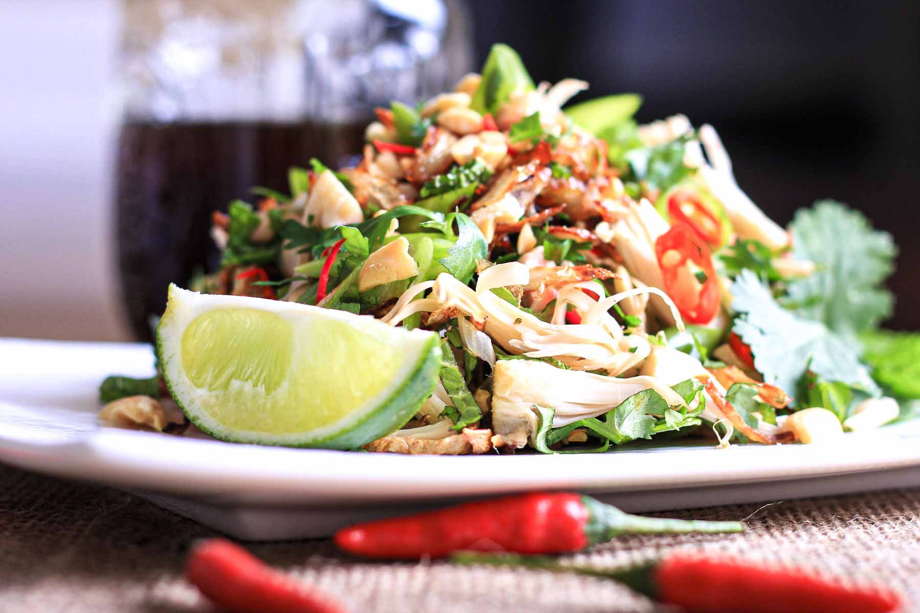 Spicy jackfruit salad topped with chili, lime, herbs, and crushed peanuts on a white plate.