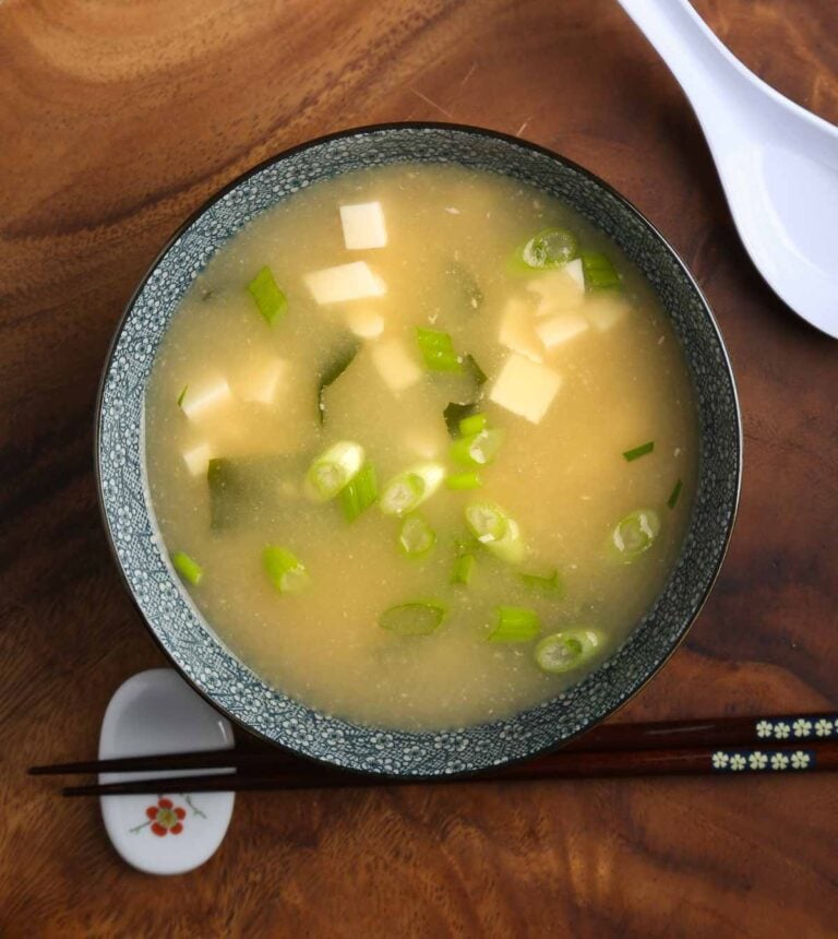 Vegan miso soup with tofu, wakame, and scallions served in a ceramic bowl on a wooden board.