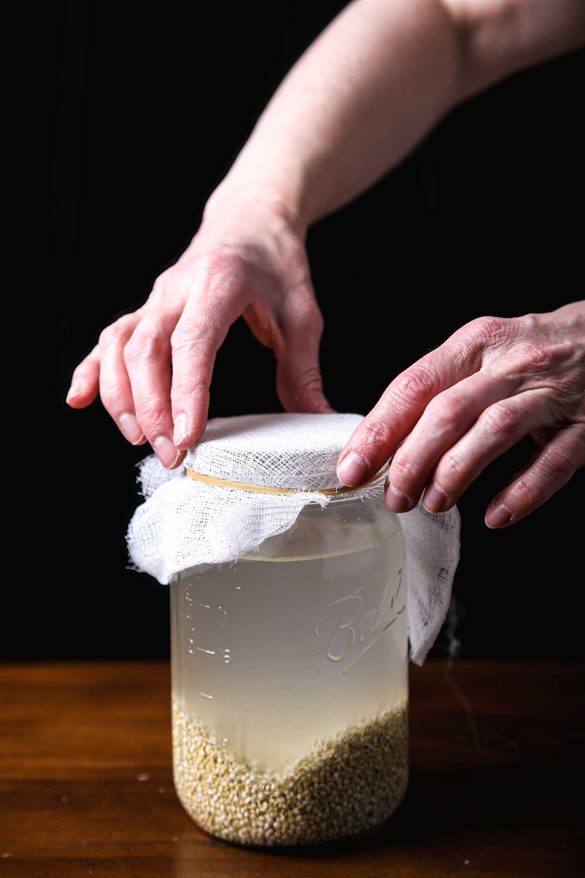 Adding a layer of cheesecloth to a mason jar with rejuvelac.